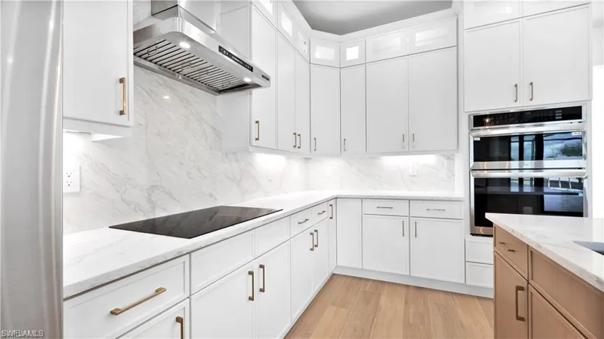 Kitchen with white cabinets, stainless steel double oven, light stone counters, and wall chimney exhaust hood