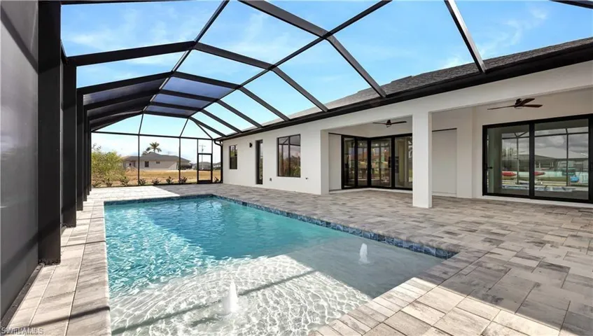 View of pool with glass enclosure, ceiling fan, and a patio area