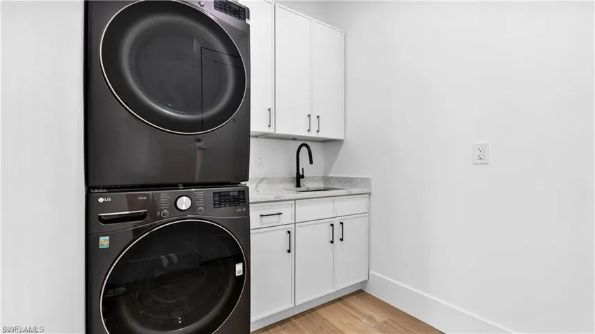 Clothes washing area with sink, cabinets, stacked washer / drying machine, and light hardwood / wood-style floors
