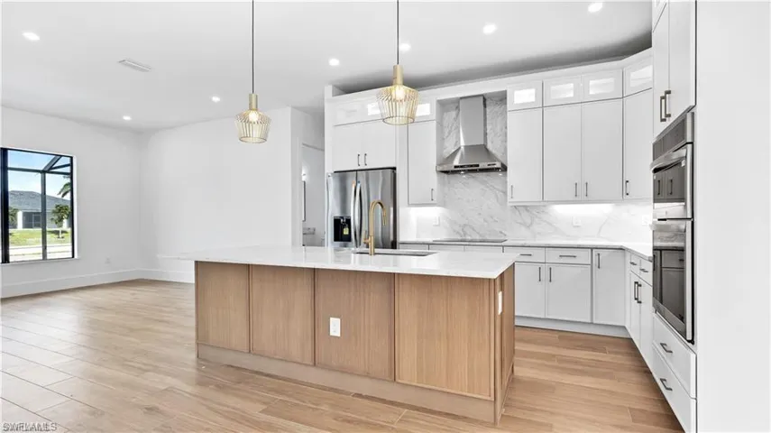Kitchen with a center island with sink, wall chimney range hood, stainless steel fridge with ice dispenser, light wood-type flooring, and white cabinetry