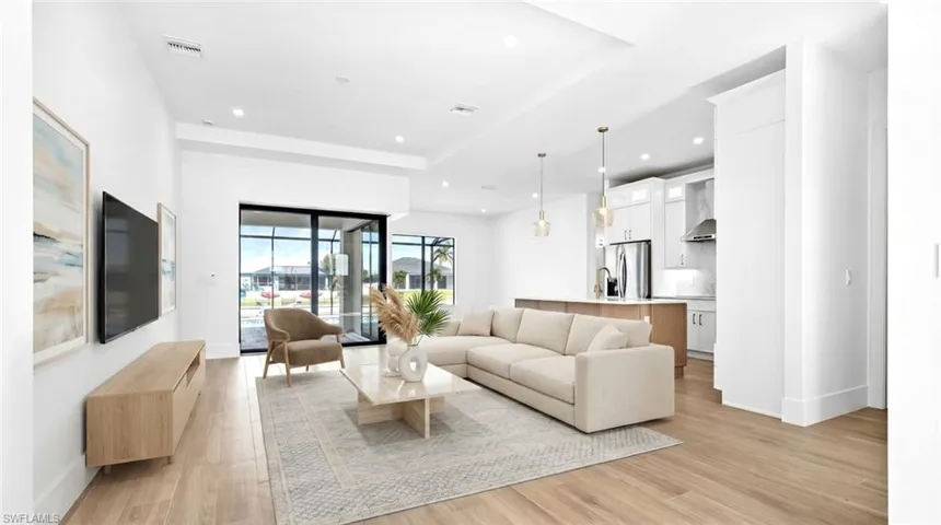 Expansive living area featuring light wood-finish flooring, recessed lighting, and a tray ceiling