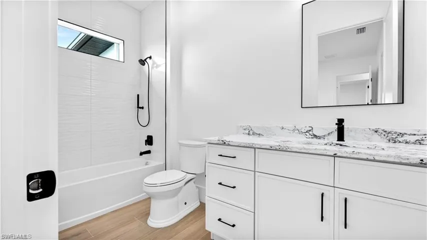 Full bathroom featuring vanity, wood-type flooring, tiled shower / bath combo, and toilet