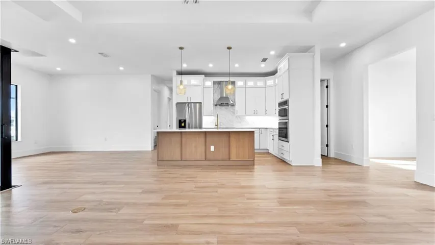 Kitchen featuring white cabinetry, wall chimney exhaust hood, stainless steel appliances, pendant lighting, and a kitchen island with sink