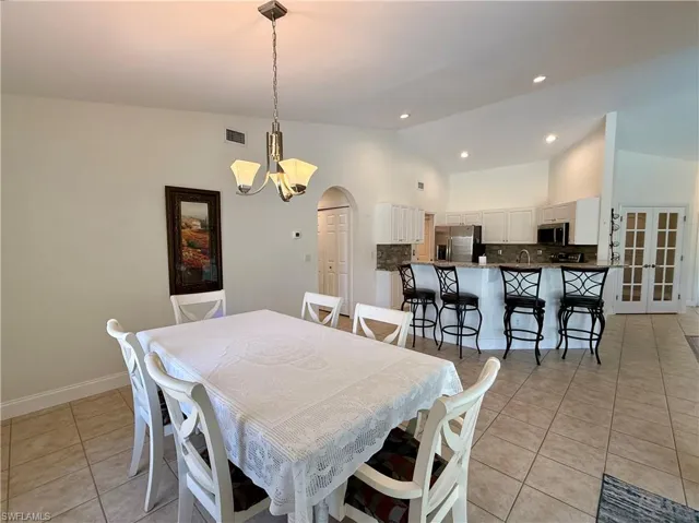 Dining room with arched walkways, light tile patterned floors, lofted ceiling, recessed lighting, and a chandelier