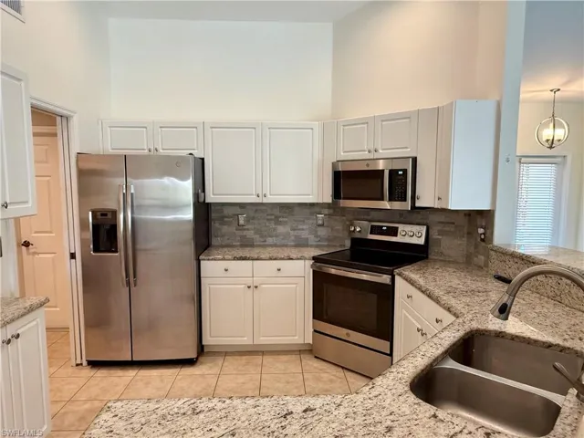 Kitchen featuring appliances with stainless steel finishes, decorative backsplash, light stone counters, and a towering ceiling