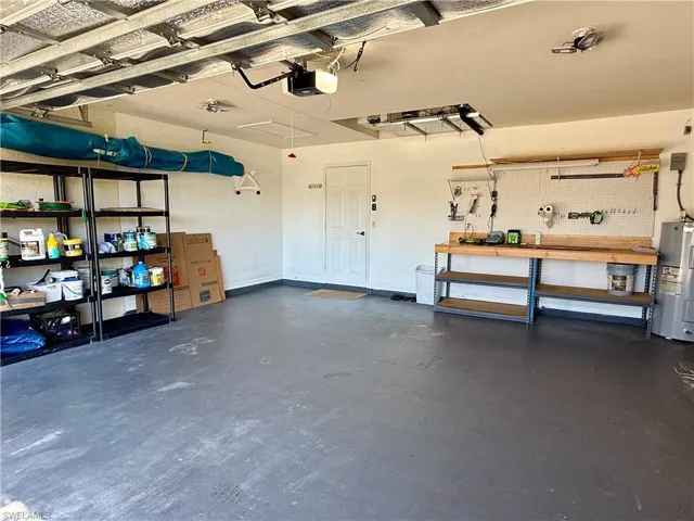Garage with a workshop area, water heater, manual shutters and a garage door opener
