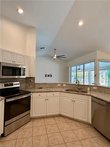 Kitchen with stainless steel appliances, vaulted ceiling, light stone counters, tasteful backsplash, and light tile patterned floors