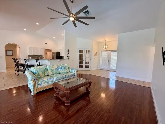Living room with french doors, arched walkways, wood finished floors, a ceiling fan, and high vaulted ceiling
