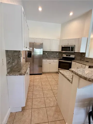 Kitchen with white cabinets, appliances with stainless steel finishes, light stone countertops, tasteful backsplash, and light tile patterned floors