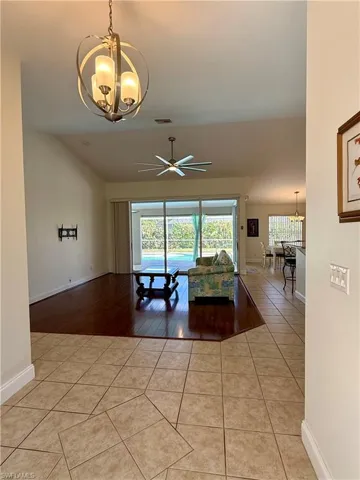 Living area featuring a chandelier, light tile patterned floors, vaulted ceiling, and ceiling fan