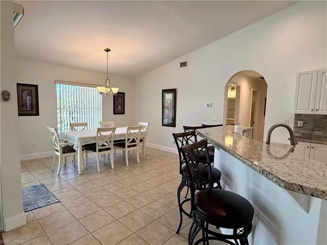Dining room with lofted ceiling, light tile patterned flooring, arched walkways, and a chandelier