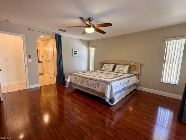Bedroom featuring arched walkways, dark wood finished floors, ceiling fan, and ensuite bath