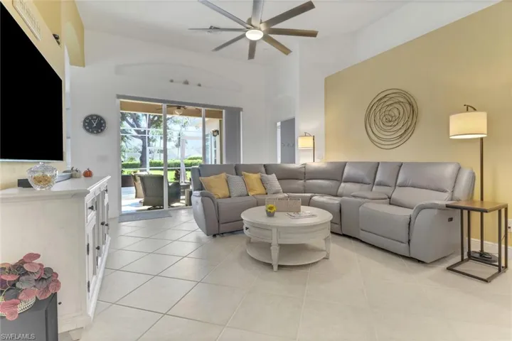 Living area featuring abundant light, tile flooring, ceiling fan, and a high ceiling with sliding glass door to the lanai