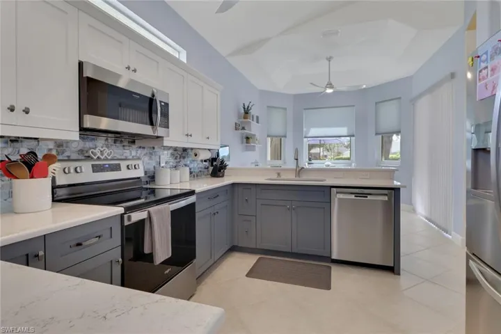 Kitchen featuring stainless steel appliances, white cabinetry, gray cabinets, ceiling fan, and tasteful backsplash, open for easy maneuvering from station to station.
