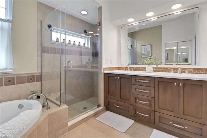 Separate bath and shower, featuring double vanity, light tile floors, a bath, and tasteful backsplash.