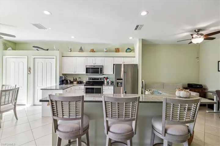 Kitchen featuring white cabinetry, appliances with stainless steel finishes, light tile patterned floors, and a kitchen bar