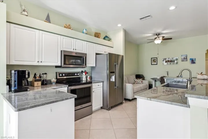 Kitchen featuring stainless steel appliances, sink, light tile patterned floors, white cabinets, and ceiling fan