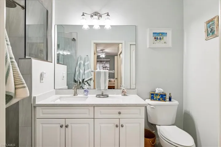 Bathroom featuring toilet, ceiling fan, vanity, and tiled shower