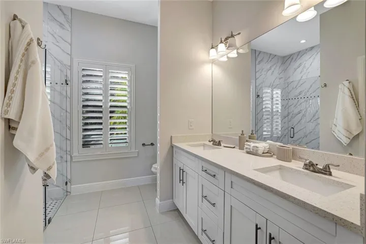 Full bathroom featuring double vanity, a marble finish shower, and light tile patterned floors