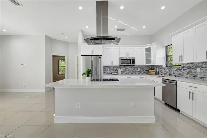 Kitchen with a kitchen island, white cabinetry, island exhaust hood, light stone countertops, and recessed lighting