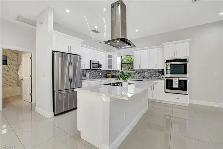 Kitchen with appliances with stainless steel finishes, white cabinetry, light stone countertops, island exhaust hood, and recessed lighting