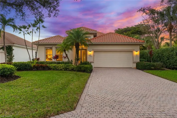 Stucco exterior with a tile roof, paver driveway, attached two-car garage, and mature landscaping