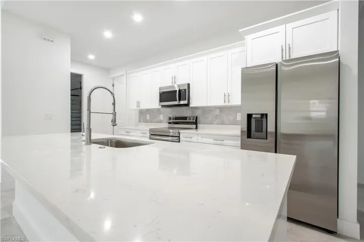 Kitchen featuring sink, stainless steel appliances, light stone counters, an island with sink, and white cabinets