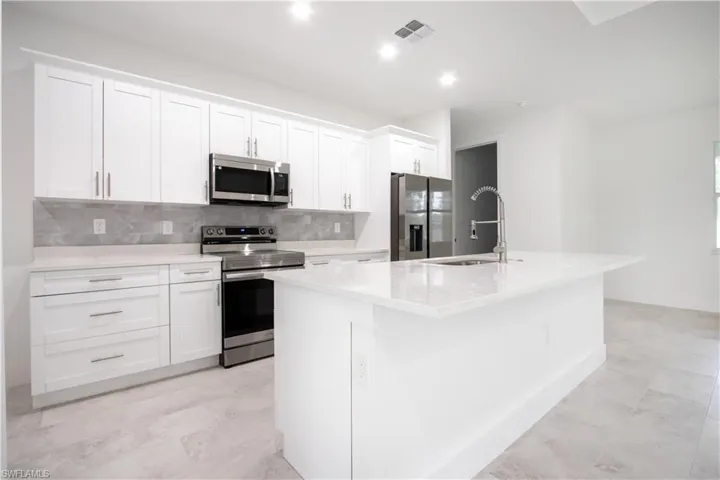 Kitchen with stainless steel appliances, white cabinetry, a kitchen island with sink, and sink