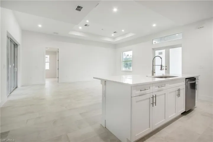 Kitchen featuring sink, white cabinetry, a center island with sink, a tray ceiling, and dishwasher