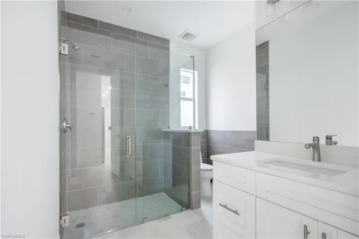 Bathroom with an enclosed shower, vanity, tile walls, and toilet