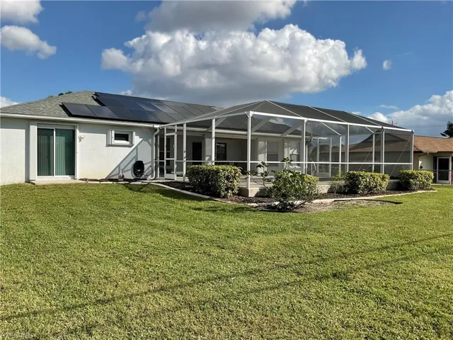 Back of property featuring a lanai, a yard, and solar panels