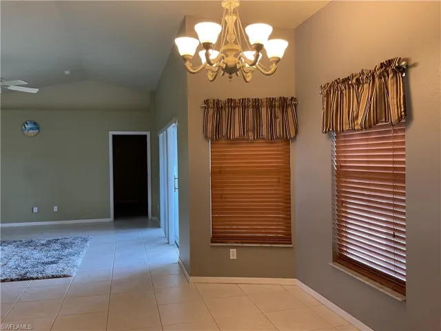 Unfurnished dining area featuring an inviting chandelier, vaulted ceiling, and light tile patterned flooring