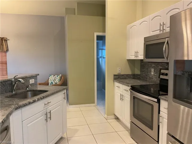 Kitchen featuring sink, stainless steel appliances, light tile patterned floors, dark stone countertops, and white cabinets