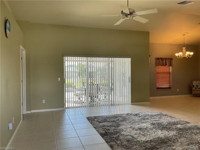 Empty room featuring tile patterned floors, ceiling fan with notable chandelier, and high vaulted ceiling