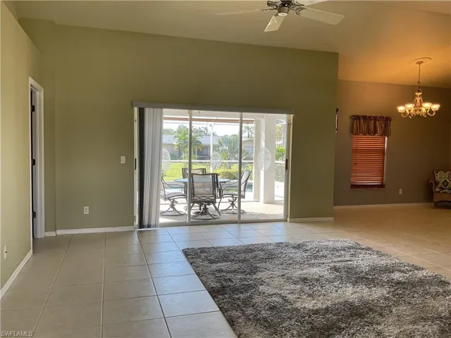 Unfurnished room featuring lofted ceiling, light tile patterned floors, and ceiling fan with notable chandelier