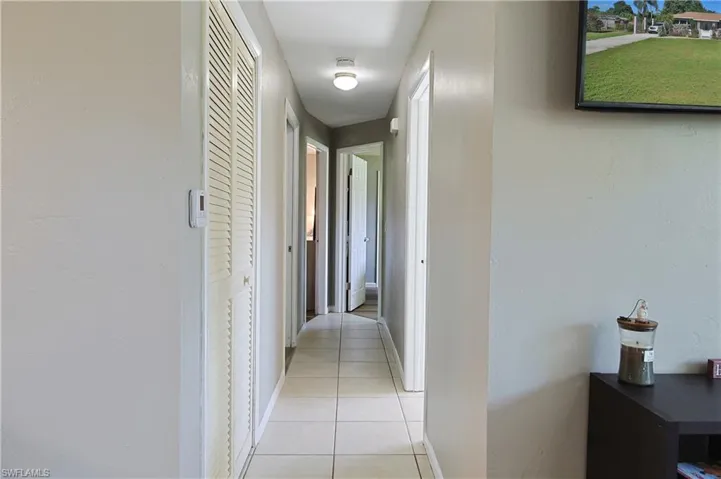 Hallway featuring neutral wall tones, tile flooring, louvered closet doors, and recessed lighting