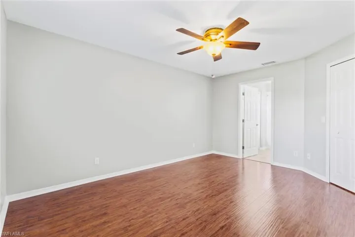 Primary bedroom with wood floors, ensuite bathroom, spacious walk in closet and lighted ceiling fan