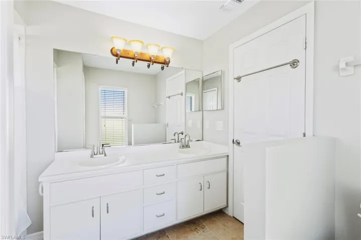 Primary shower / bathtub combination with double vanity, and neutral tile patterned floors