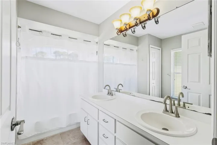 Primary full bathroom with shower / bathtub combination with double vanity, and neutral tile patterned floors