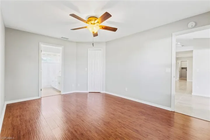 Primary bedroom with wood floors, ensuite bathroom, spacious walk in closet and lighted ceiling fan