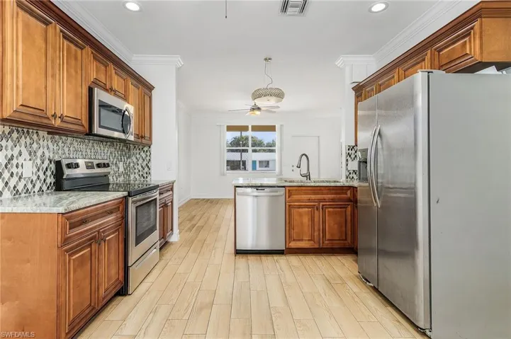 Kitchen featuring appliances with stainless steel finishes, a peninsula, light stone counters, brown cabinets, and crown molding