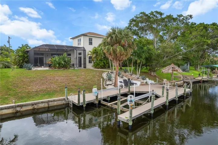 Dock featuring a water view, boat lift, glass enclosure, and a yard