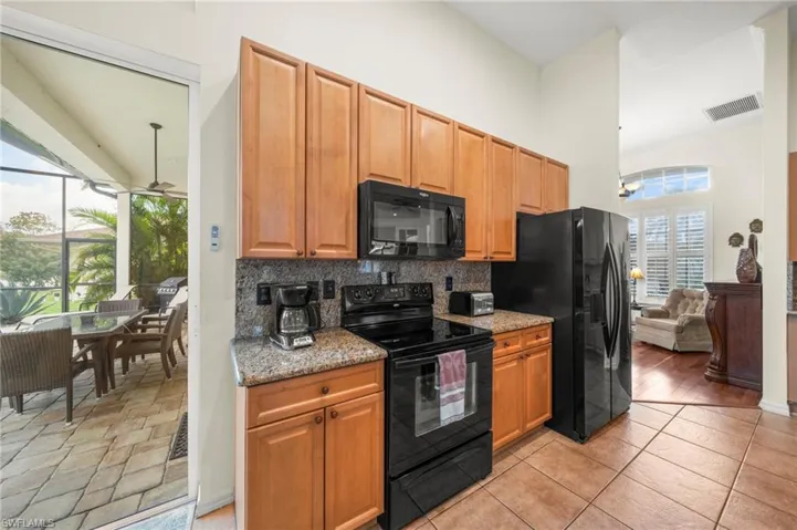 Kitchen featuring black appliances, light stone countertops, ceiling fan, wood finish cabinetry, and backsplash
