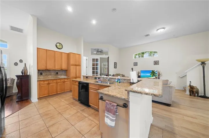Kitchen featuring a ceiling fan, black appliances, open floor plan, light stone counters, and tasteful backsplash