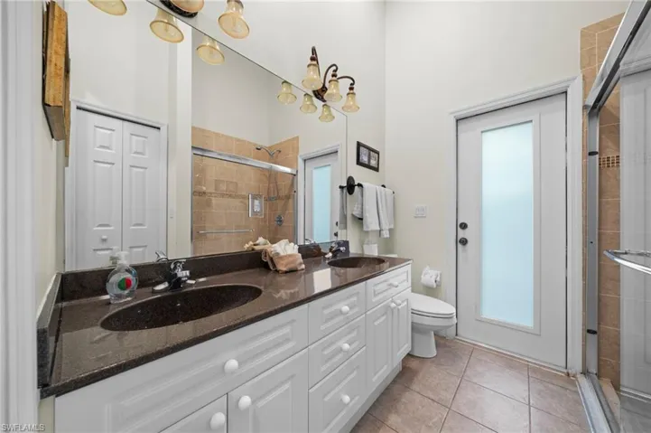 Full bathroom with double vanity, light tile patterned floors, a shower stall, and a high ceiling