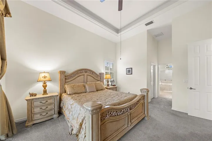 Carpeted bedroom featuring a raised ceiling, ceiling fan, and ensuite bathroom