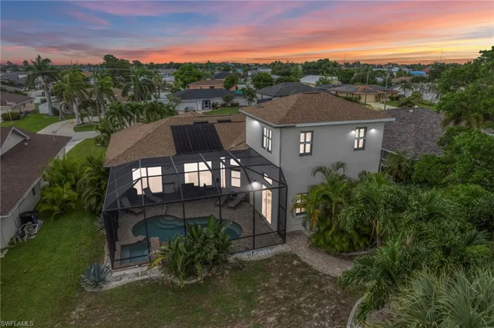 Back of house at dusk with a sunroom, a shingled roof, stucco siding, glass enclosure, and an outdoor pool