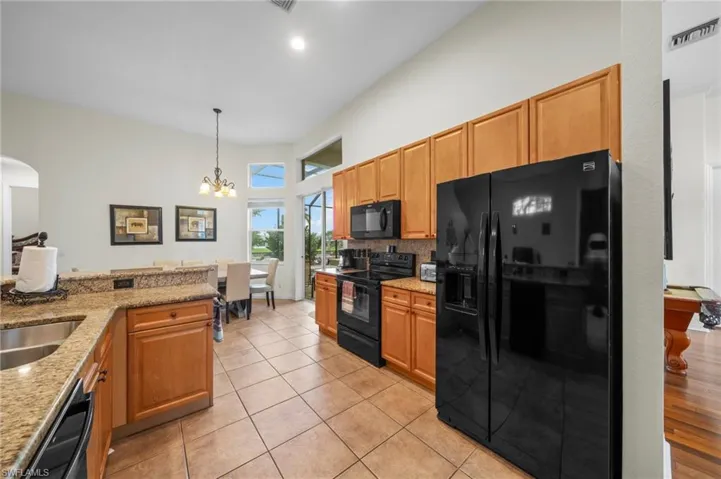 Kitchen with black appliances, light stone counters, light tile patterned floors, hanging lights, and a high ceiling