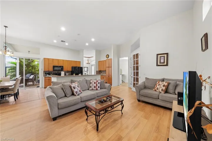 Living room with suspended lighting, light wood-type flooring, and a high ceiling
