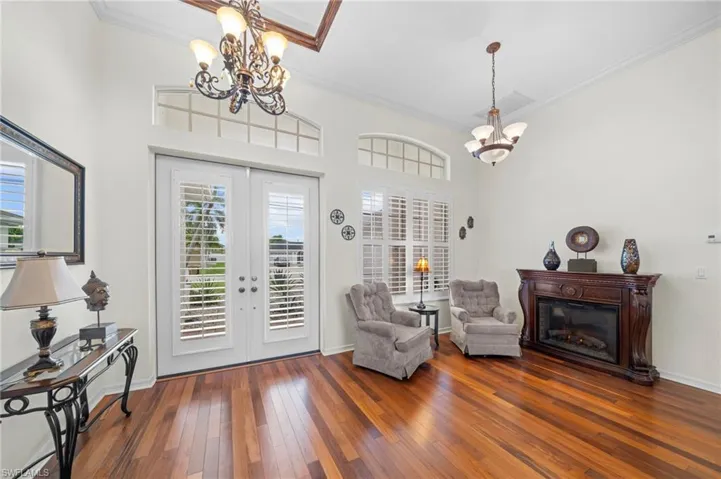 Sitting room featuring suspended lighting, crown molding, french doors, hardwood / wood-style flooring, and a glass covered fireplace